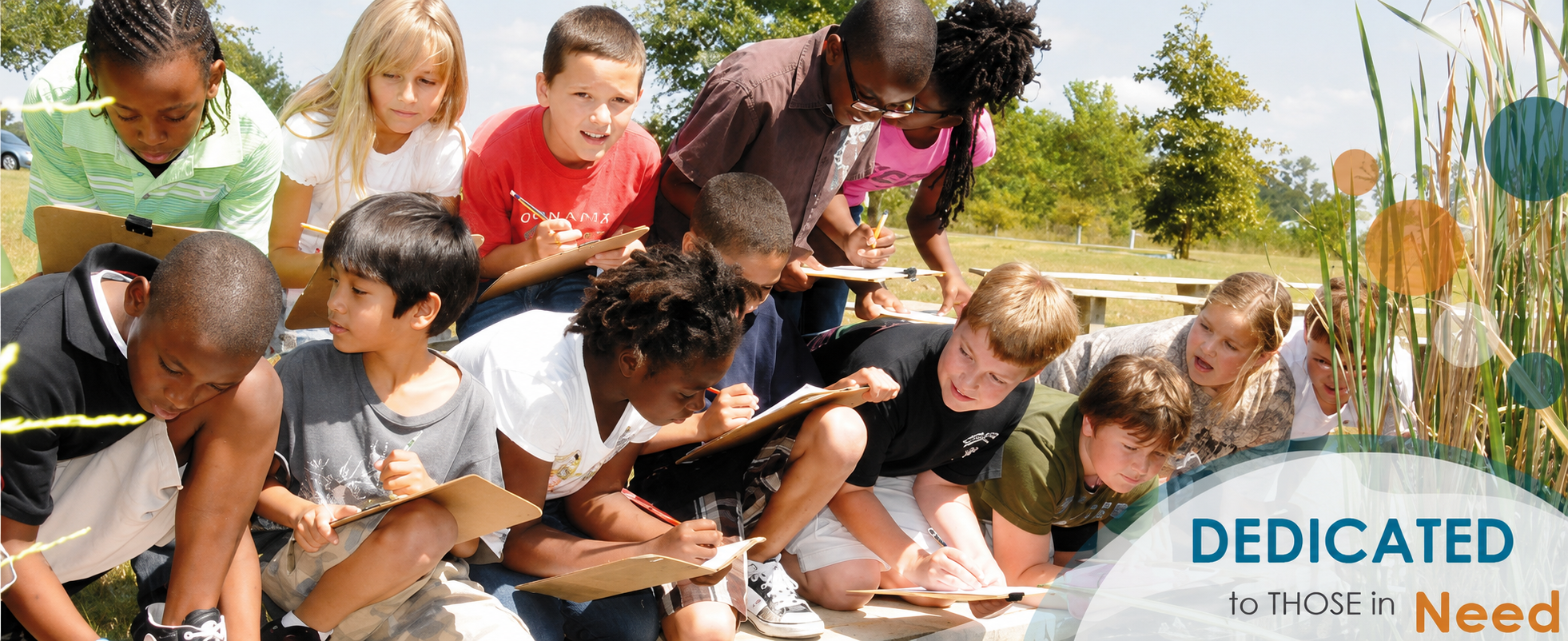 Schoolchildren gathered outdoors around an instructor near water and reeds